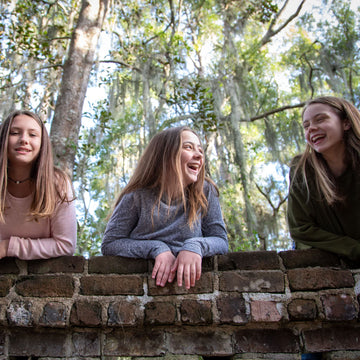 tweens hanging over a brick wall laughing and smiling