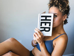 girl sitting in a chair with a book covering part of her face - Nipple Piercing Bra