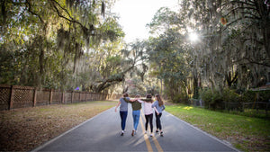 teens and tween girls with arms around each other walking down a tree lined street