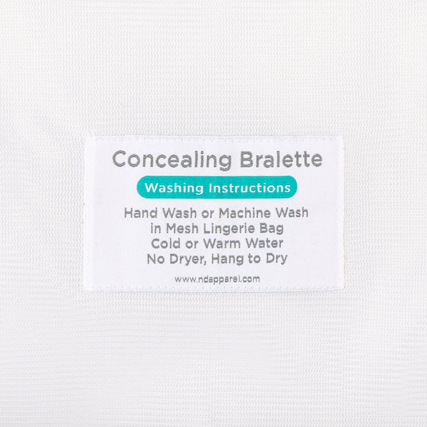 Close-up of the laundry care label on a mesh bag outlining instructions to hand wash or machine wash concealing bralettes in cold or warm water and hang dry.