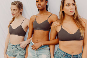 three girls standing with linked arms in nipple concealing bralettes and jean shorts